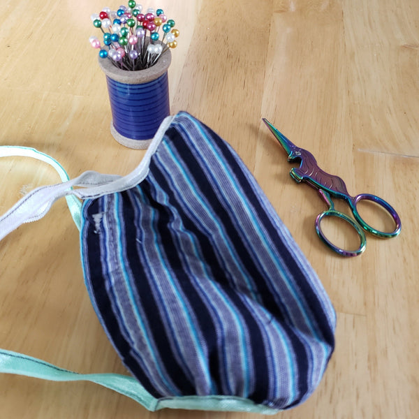 Striped face mask on table with pins and scissors.